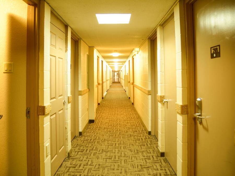 A hotel hallway with carpeted floors, wooden doors, and a ceiling light.