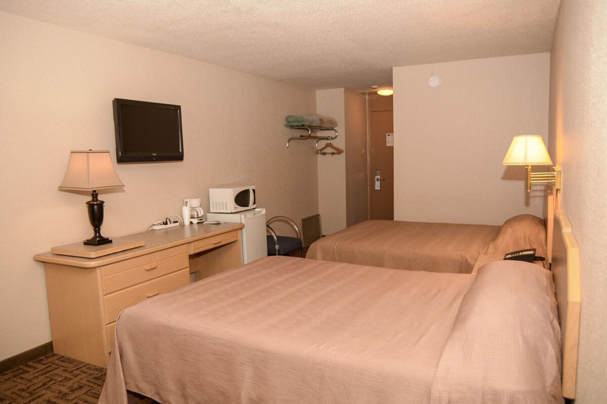 A hotel room with two beds, a desk with a lamp, a microwave, and a TV on the wall.