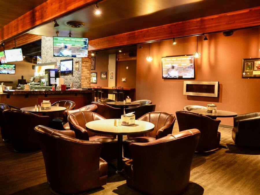 Un restaurante con asientos de cuero, una zona de bar y varias televisiones mostrando deportes.