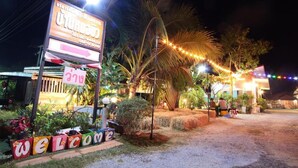 Un espacio exterior bien iluminado con un cartel de 'WELCOME', una palmera y luces colgantes.