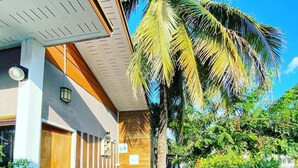 Un edificio moderno con una puerta de madera, una pequeña mesa exterior con diseño de sandía y una palmera.
