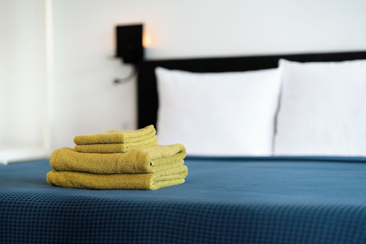 Un montón de toallas dobladas con cuidado sobre una cama con cubrecama azul y cabecera negra.
