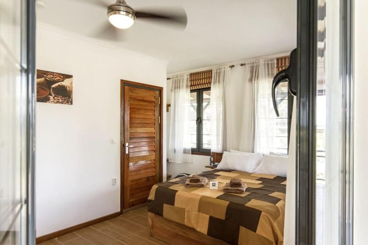 Un dormitorio con una cama, una puerta de madera, un ventilador de techo y una ventana con cortinas.