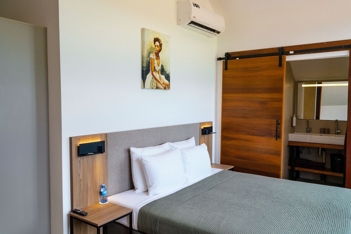 Habitación de hotel con una cama, un cuadro, aire acondicionado, un armario de madera y un baño con espejo.