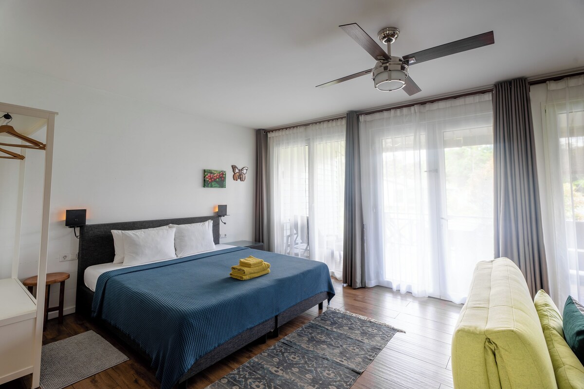 Una habitación de hotel con cama, mesita de noche y ventilador de techo.