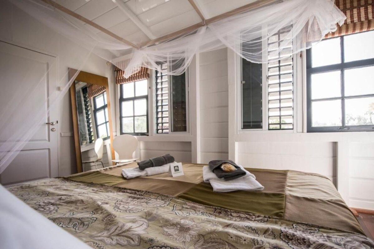 Una habitación con una cama, una silla, una ventana con contraventanas y una puerta.