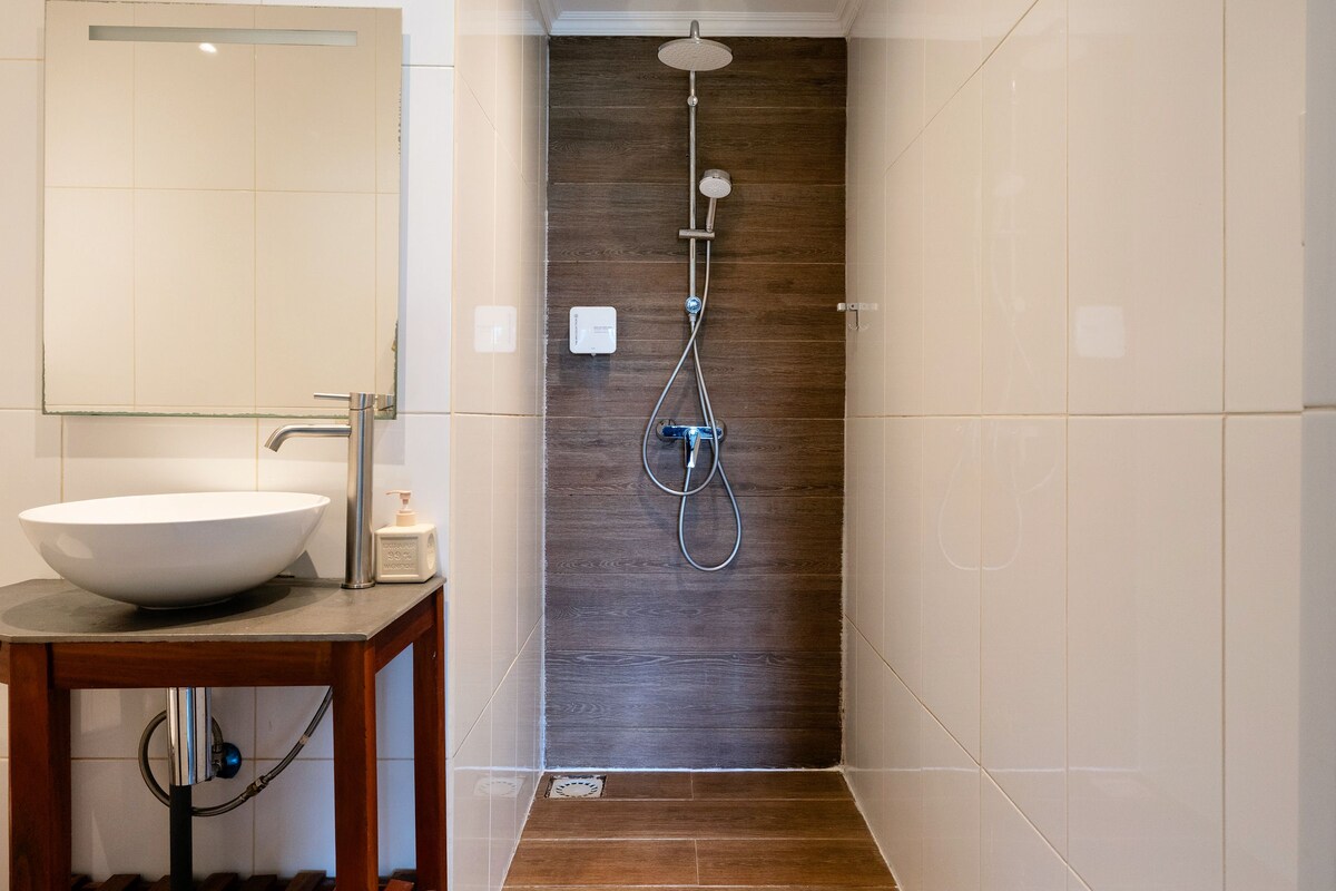 Un baño moderno con tocador de madera, un espejo grande y zona de ducha.