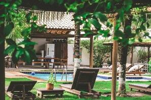 Zona de piscina con sillas de descanso, una mesa pequeña con una planta y un área de estar cubierta con techo de baldosas.
