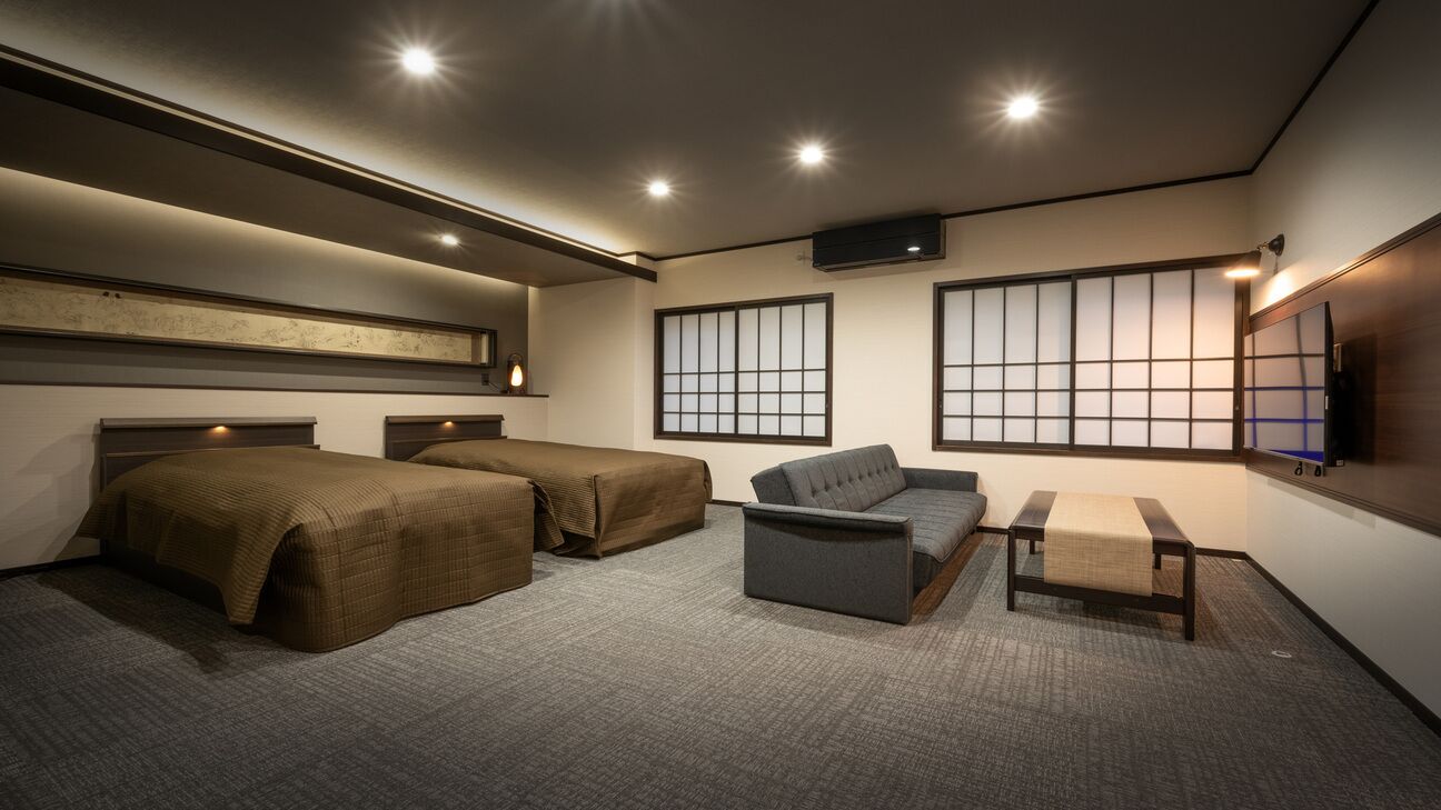 A hotel room with two beds, a sofa, a small table, and a TV.