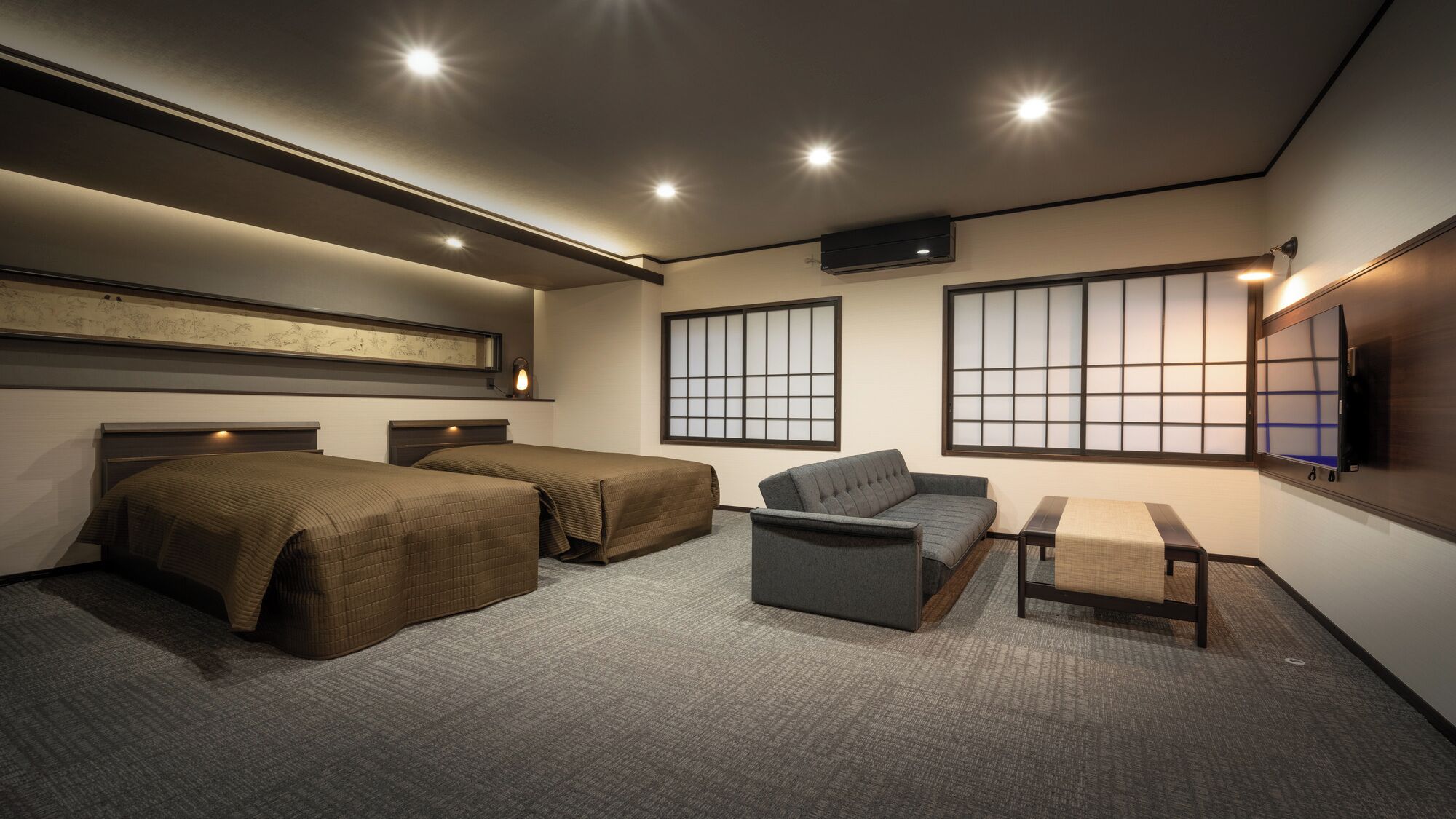 A hotel room with two beds, a sofa, a small table, and a TV.