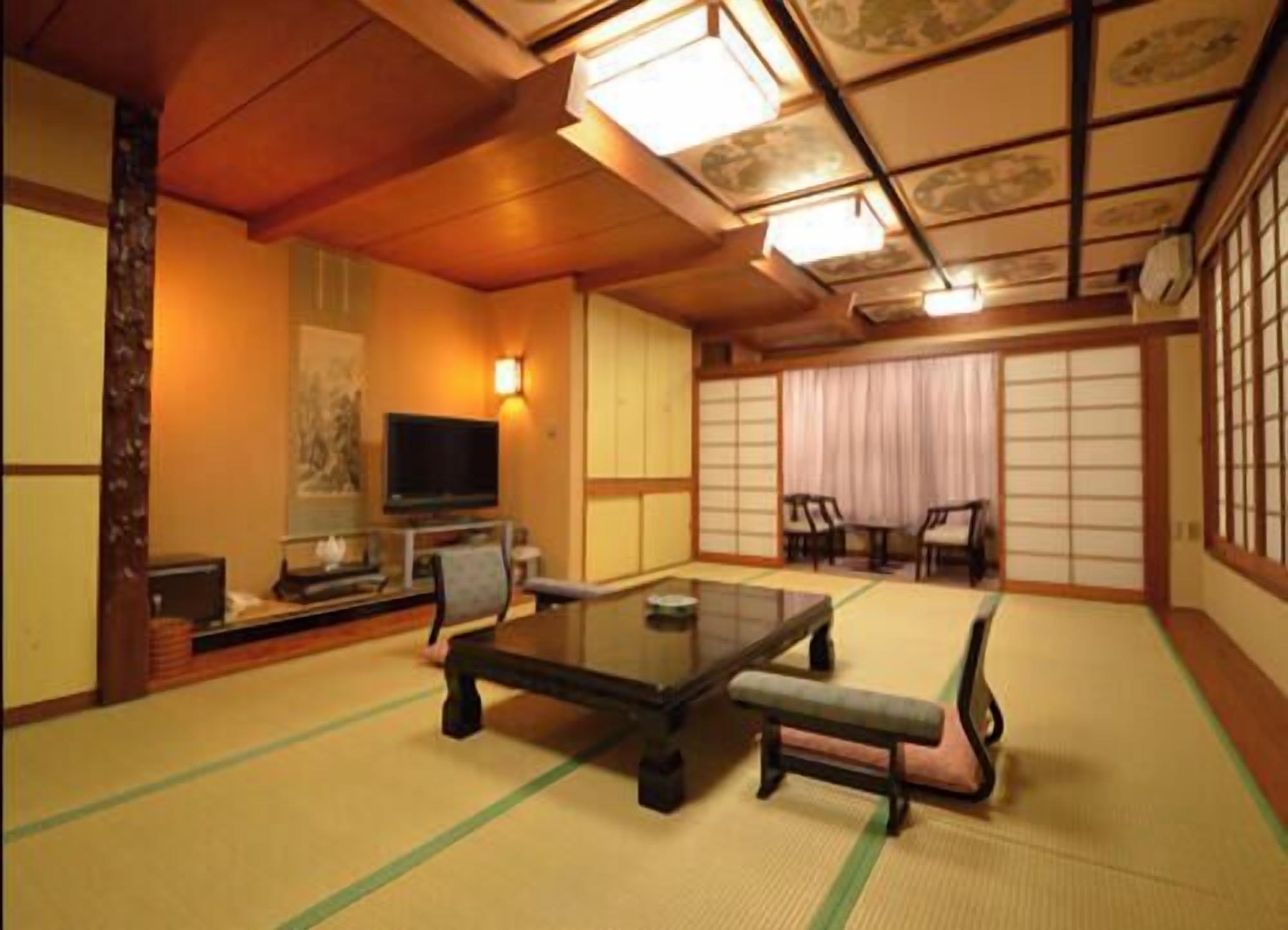 A traditional Japanese room with tatami flooring, a low table, chairs, a television, and sliding doors.