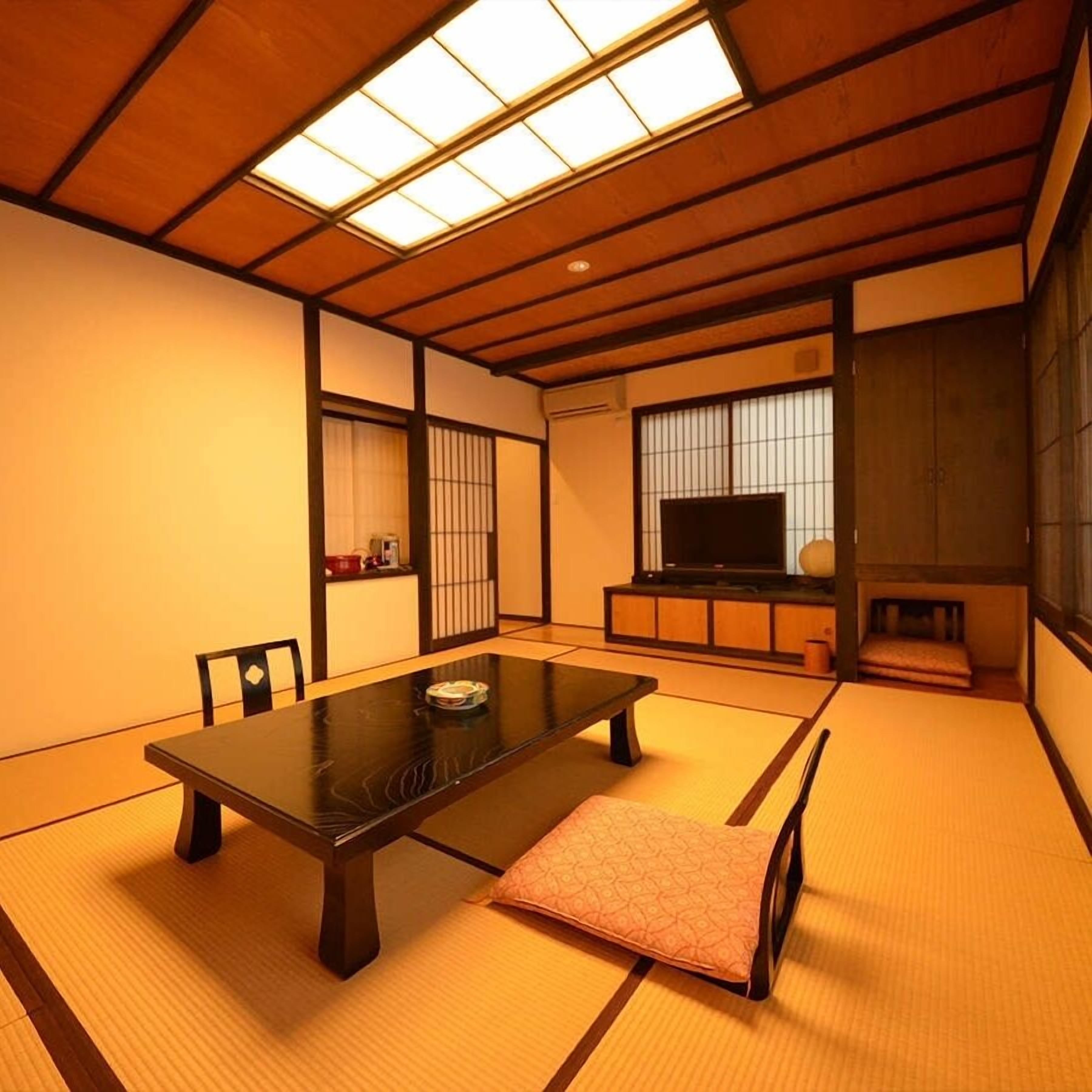 A traditional Japanese room with tatami flooring, a low table, a sofa, a television, and sliding doors.