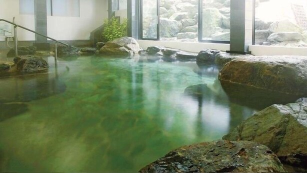 Un área de aguas termales con agua cristalina, rocas y una escalera que sube.