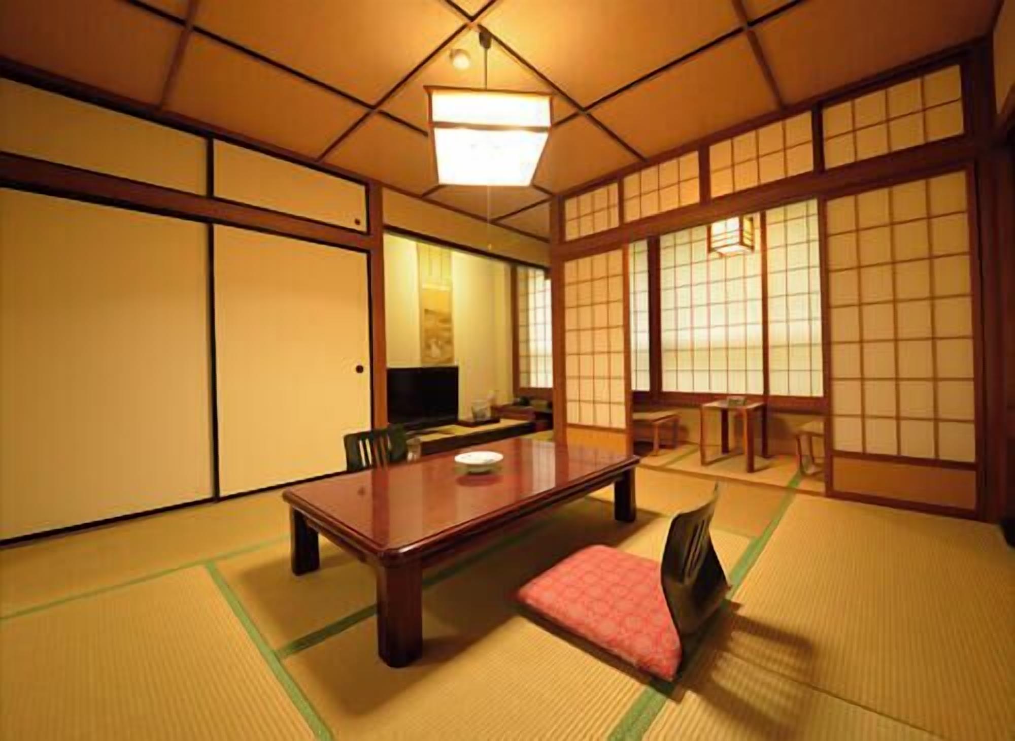 A traditional Japanese room with tatami flooring, a low table, a television, and sliding doors.
