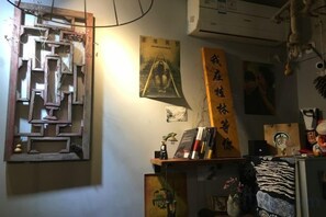 A room with a wall-mounted abstract art piece, a framed poster, and a shelf with various items including books and decorative objects. - I am waiting for you in Guilin Youth Hostel (Liangjiang Sihu East-West Alley) (Guilin)