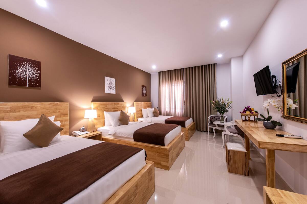 Une chambre d’hôtel avec trois lits en bois, un bureau, une chaise et un téléviseur fixé au mur.