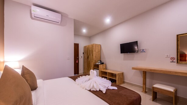 Quarto de hotel com uma cama, guarda-roupa de madeira, televisão, escrivaninha e um banco.