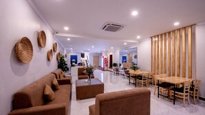 A modern hotel lobby with brown sofas, a wooden dining table, and woven wall art. - Double S Hotel (Battambang)