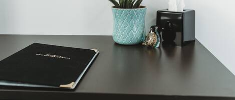 A desk with a black folder, a turquoise plant, a tissue box, and a decorative glass bottle.