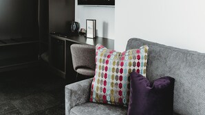 A modern living room with a grey sofa, a colorful geometric pillow, and a dark coffee table. - Coniston Hotel Wollongong (Coniston)