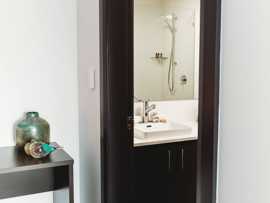 A bathroom with a white sink, a glass shelf with toiletries, and a shower with a handheld showerhead.