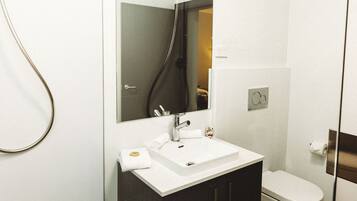 A modern bathroom with a white sink, dark cabinets, a glass shower enclosure, and a toilet.