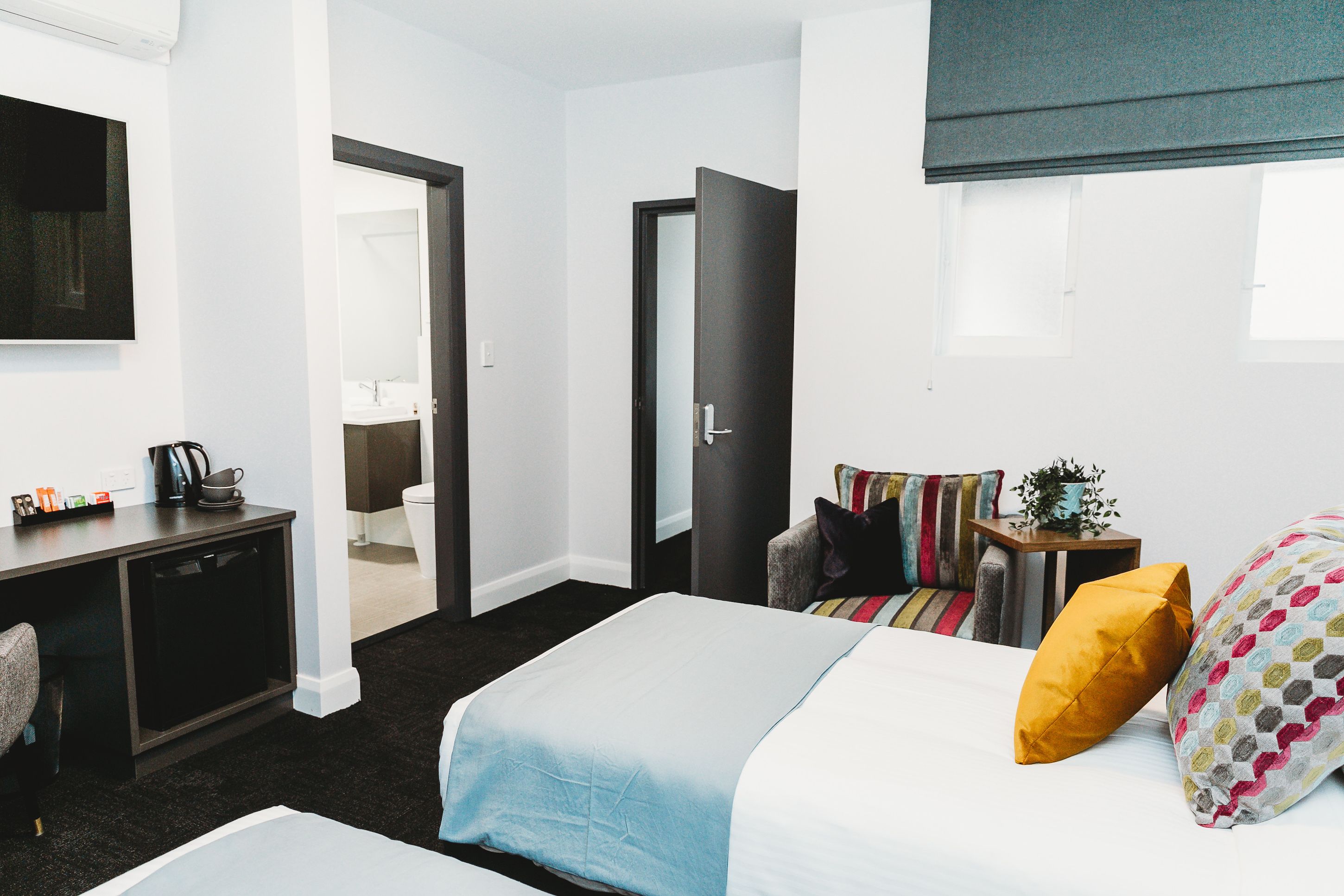 A hotel room with a bed, bedside table, and a desk with a chair. There is a window with a view of the outside.
