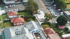 A multi-story building with a curved roof, a parking lot, and several adjacent houses. - Coniston Hotel Wollongong (Coniston)