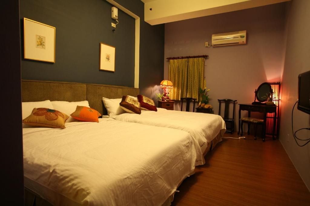 A hotel room with two beds, a desk with a chair, a mirror, and an air conditioning unit on the wall.