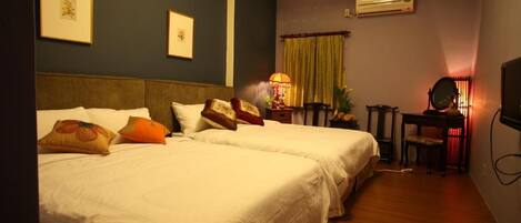 A hotel room with two beds, a desk with a chair, a mirror, and an air conditioning unit on the wall.