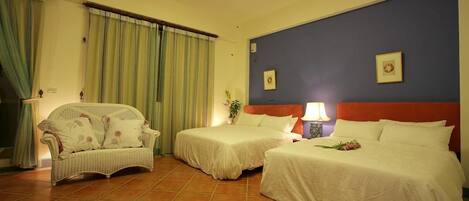 Habitación de hotel con dos camas, un sofá y una mesita de noche con lámpara.