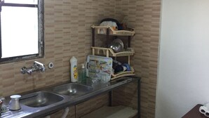 Una cocina pequeña con un lavamanos, una ventana y un estante con vajilla y productos de limpieza.