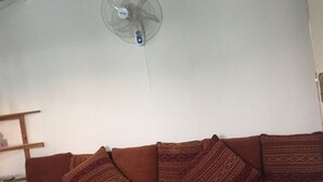 Un salón con un sofá marrón, cojines estampados y un ventilador de techo.