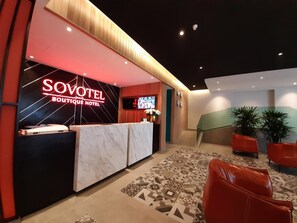A hotel reception area with a modern design, a reception desk, a TV screen, and a staircase leading to another floor. - Sovotel Conezion Putrajaya (Serdang)