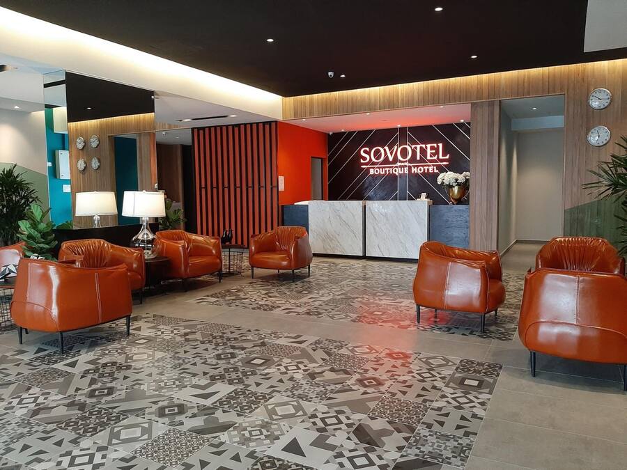 A lobby with leather chairs, a patterned carpet, and a reception desk with a 'SOVOTEL BOUTIQUE HOTEL' sign.