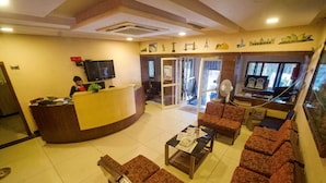A reception area with a counter, seating, and a television. - Kaveri Hotel (Mysore)