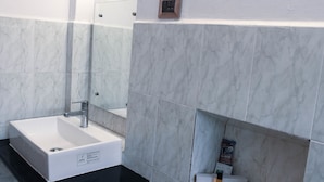 A bathroom with a white sink, black countertop, and marble tiles. - Kaveri Hotel (Mysore)