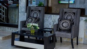 Two intricately designed chairs with a glass coffee table in a lobby area with marble walls and a television mounted on the wall. - Londa Hotel (Port Harcourt)
