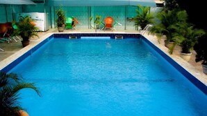 A rectangular indoor swimming pool with a tiled edge, surrounded by potted plants and colorful chairs. - Londa Hotel (Port Harcourt)