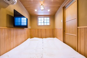 A hotel room with a bed, a TV mounted on the wall, a window, and wooden paneling on the walls.