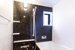 A modern bathroom with a black marble wall, a white bathtub, a shower with a handheld showerhead, and a small window with a black frame.