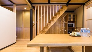 Eine Holztreppe mit Geländer, ein Holztisch mit Korb und Flaschen sowie eine Mikrowelle auf einem Regal.