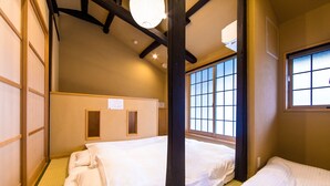 Ein traditioneller japanischer Raum mit Tatami-Böden, niedriger Decke mit dunklen Balken und einem großen Fenster mit Gittermuster.