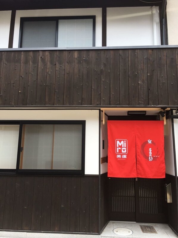 A building with a dark wooden facade and white walls. There is a red banner with white text hanging on the right side.