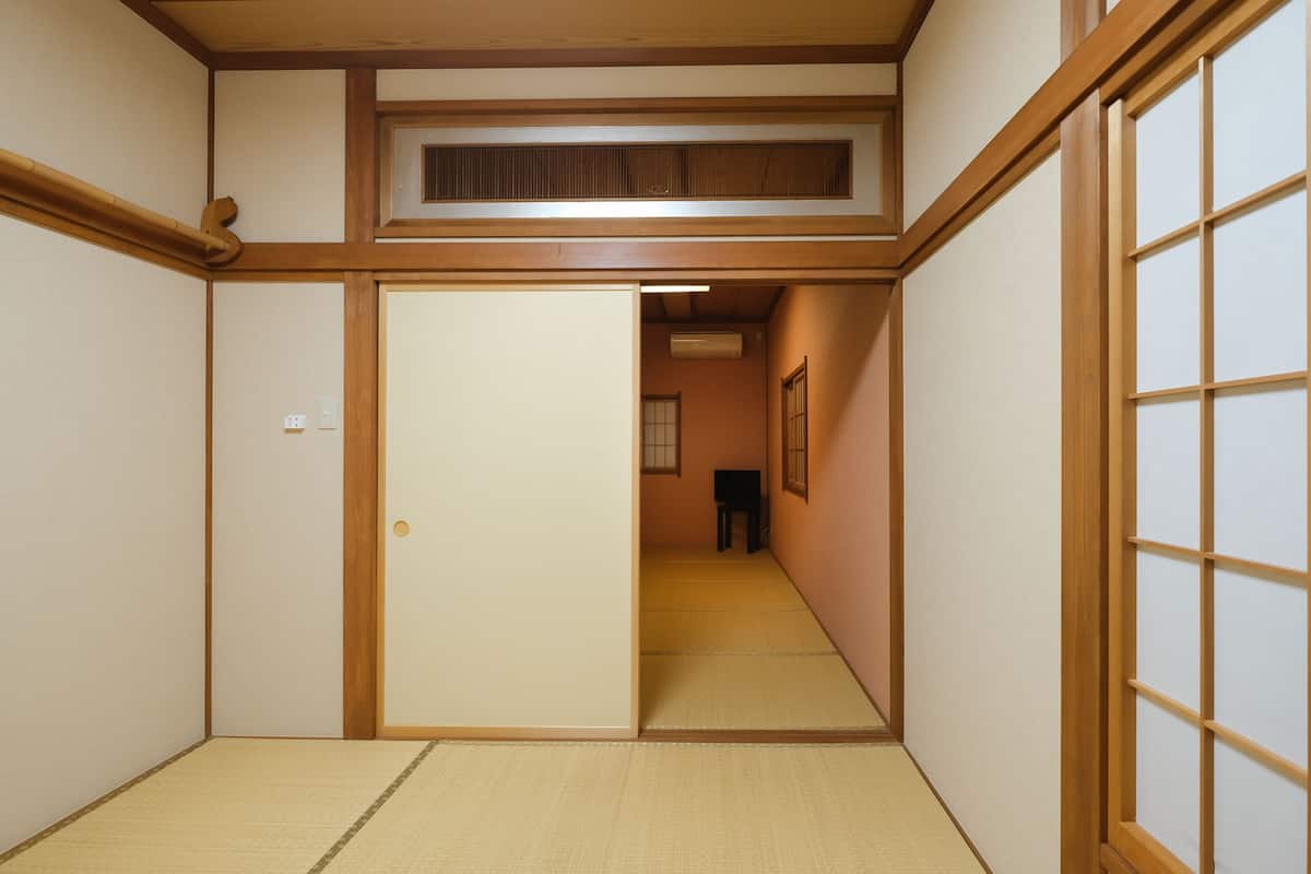 Ein traditioneller japanischer Raum mit Tatami-Boden, einer Schiebetür und einem kleinen Fenster mit Holzrahmen.