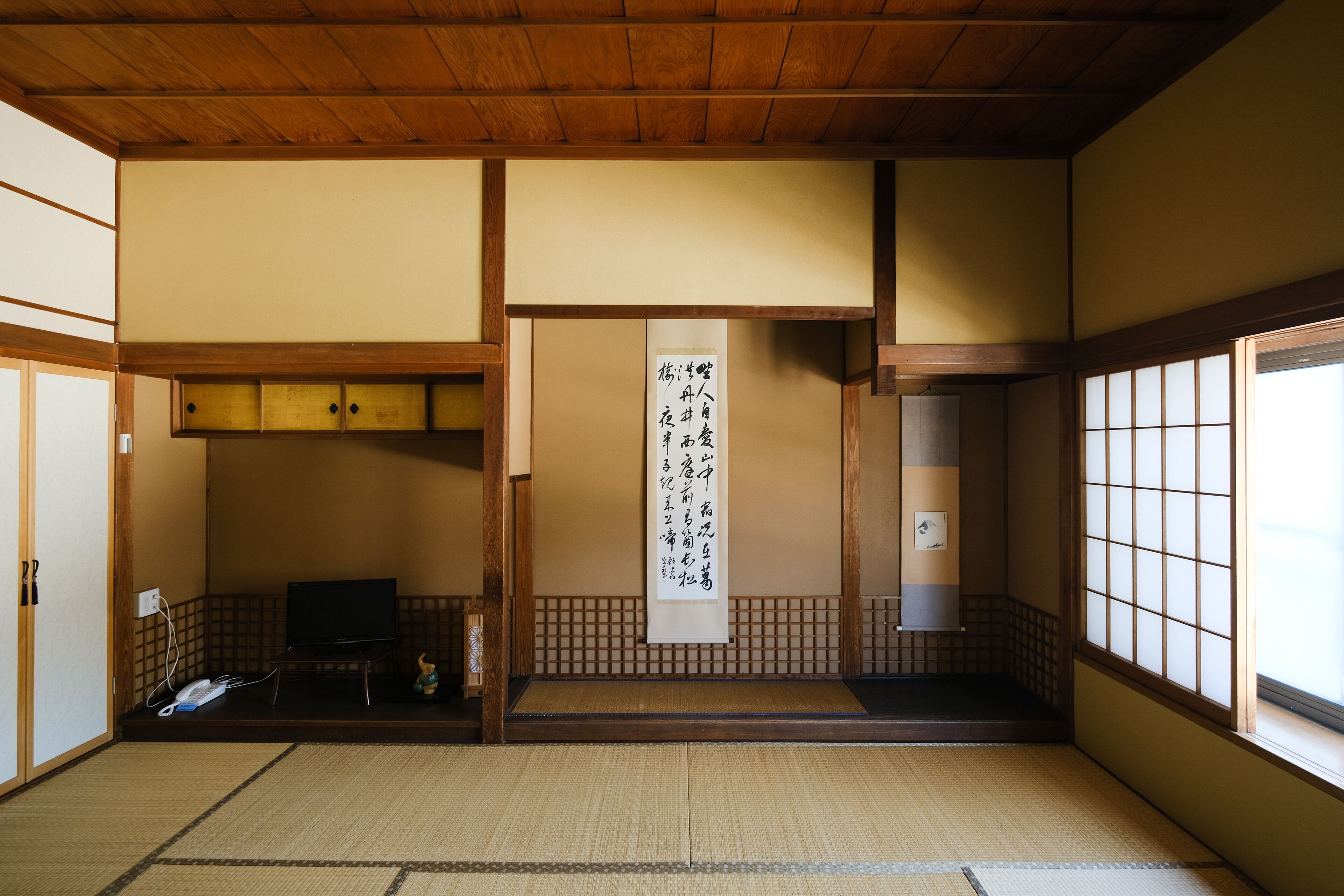 A traditional Japanese room with tatami flooring, a shoji screen, a tatami mat in the center, and a television on a low table.