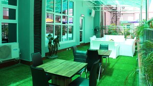 Un restaurant à la décoration intérieure verdoyante, doté de grandes fenêtres et d’un espace extérieur aménagé avec des places assises couvertes.