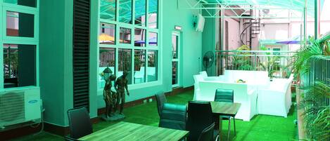 A restaurant with a green interior, large windows, and a covered outdoor seating area.