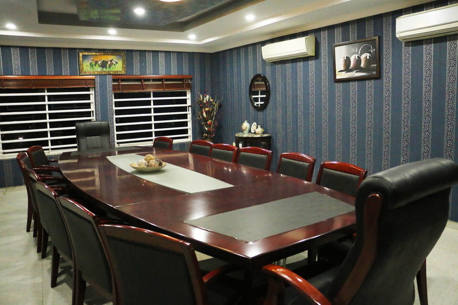 A conference room with a large rectangular table, multiple chairs, and a decorative vase on a side table.