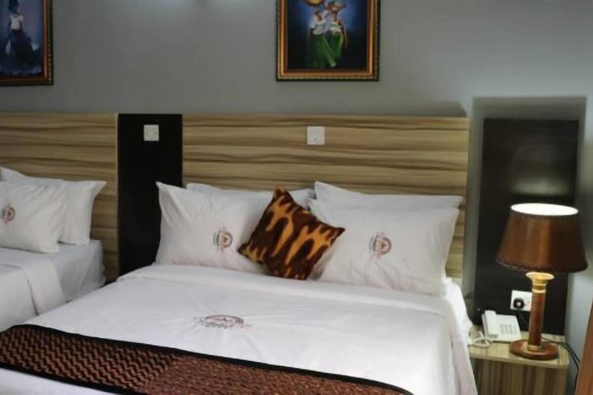 Quarto de hotel com duas camas, mesa de cabeceira com abajur e obras de arte nas paredes.